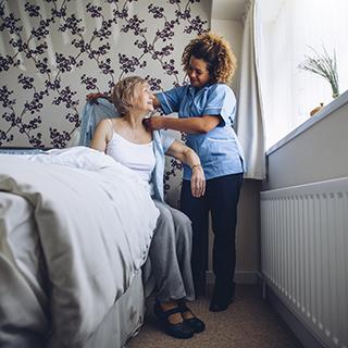 person with dementia sitting at side of bed getting help from a home health aide